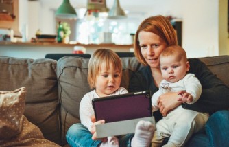 two babies and woman sitting on sofa while holding a tablet