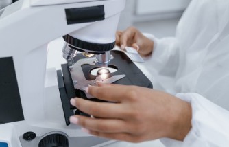A Person in White Robe using a Microscope