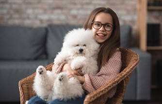 Happy girl in eyeglasses sitting with dog in wicker chair