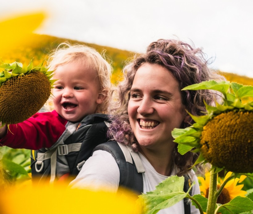 woman in white shirt carrying baby in yellow sunflower field during daytime