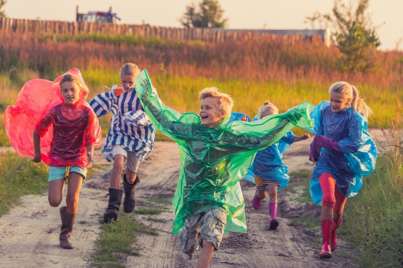 Children in colorful raincoats running laughing along the footpath